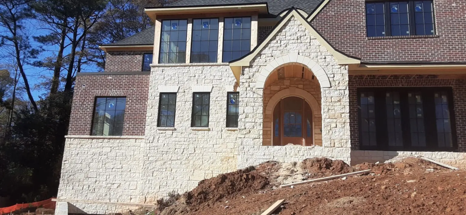 Brick and light-stone residential facade with unfinished grading in front of the entry