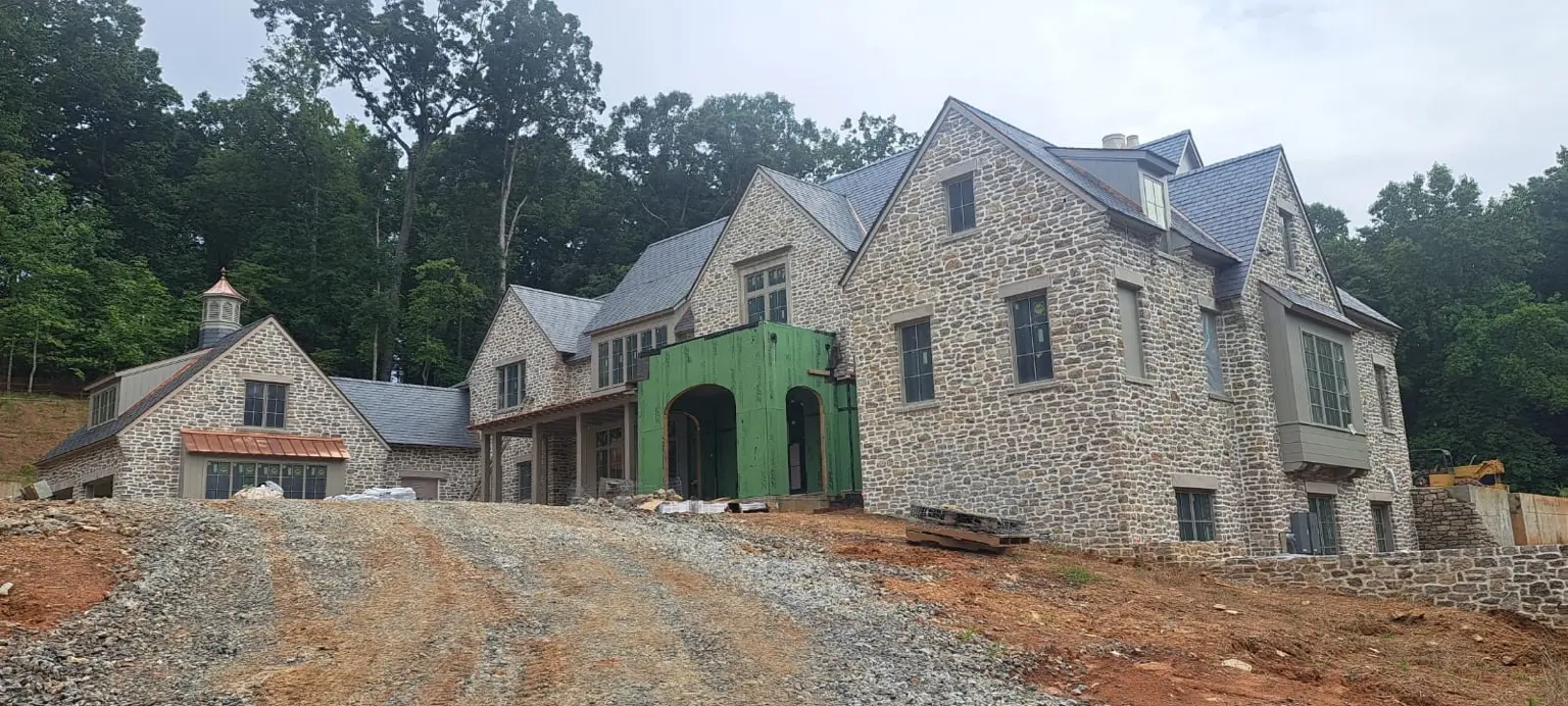 Large stone-clad residence under construction with an unfinished front entry and graded approach