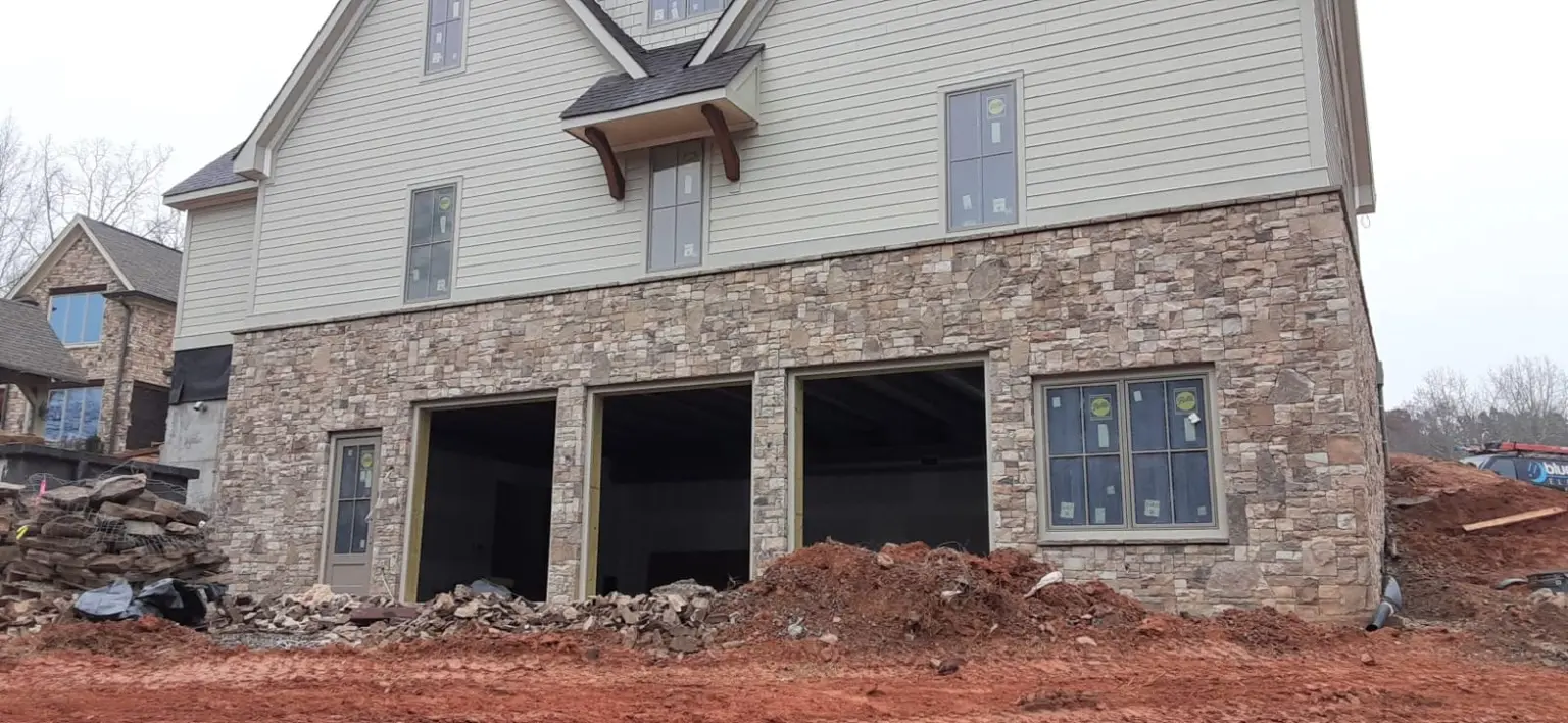New home's stone-clad garage level and upper siding during exterior construction