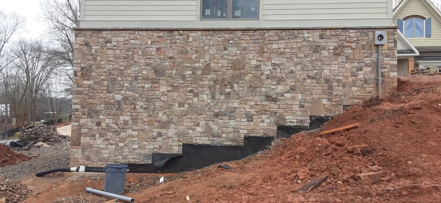 Stone-clad side elevation of a residence above an unfinished sloped site