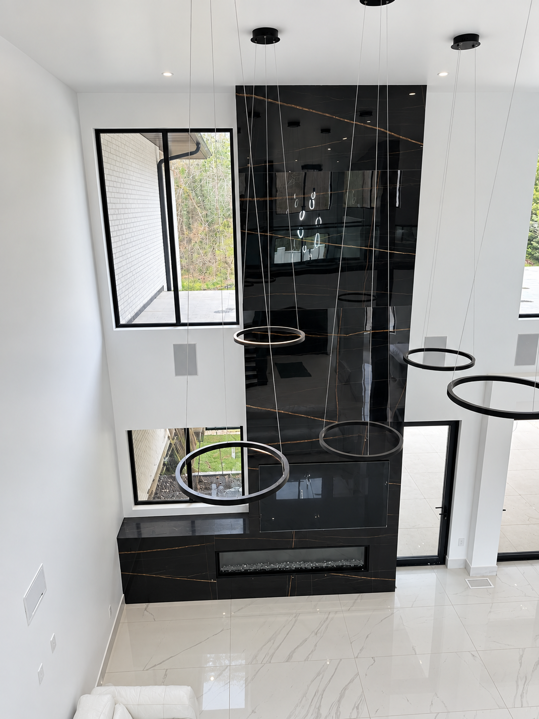 Tall dark stone fireplace wall with modern ring lights and white tile floor